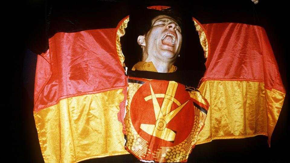 Ein Mann schaut durch das herausgeschnittene Emblem der DDR-Fahne. 