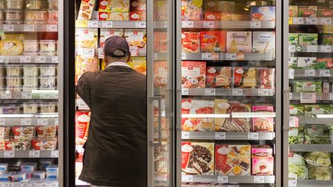 Ein Mann im Supermarkt bedient sich am Tiefkühlregal