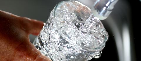 Wasser fließt aus einem Wasserhahn in ein Glas.